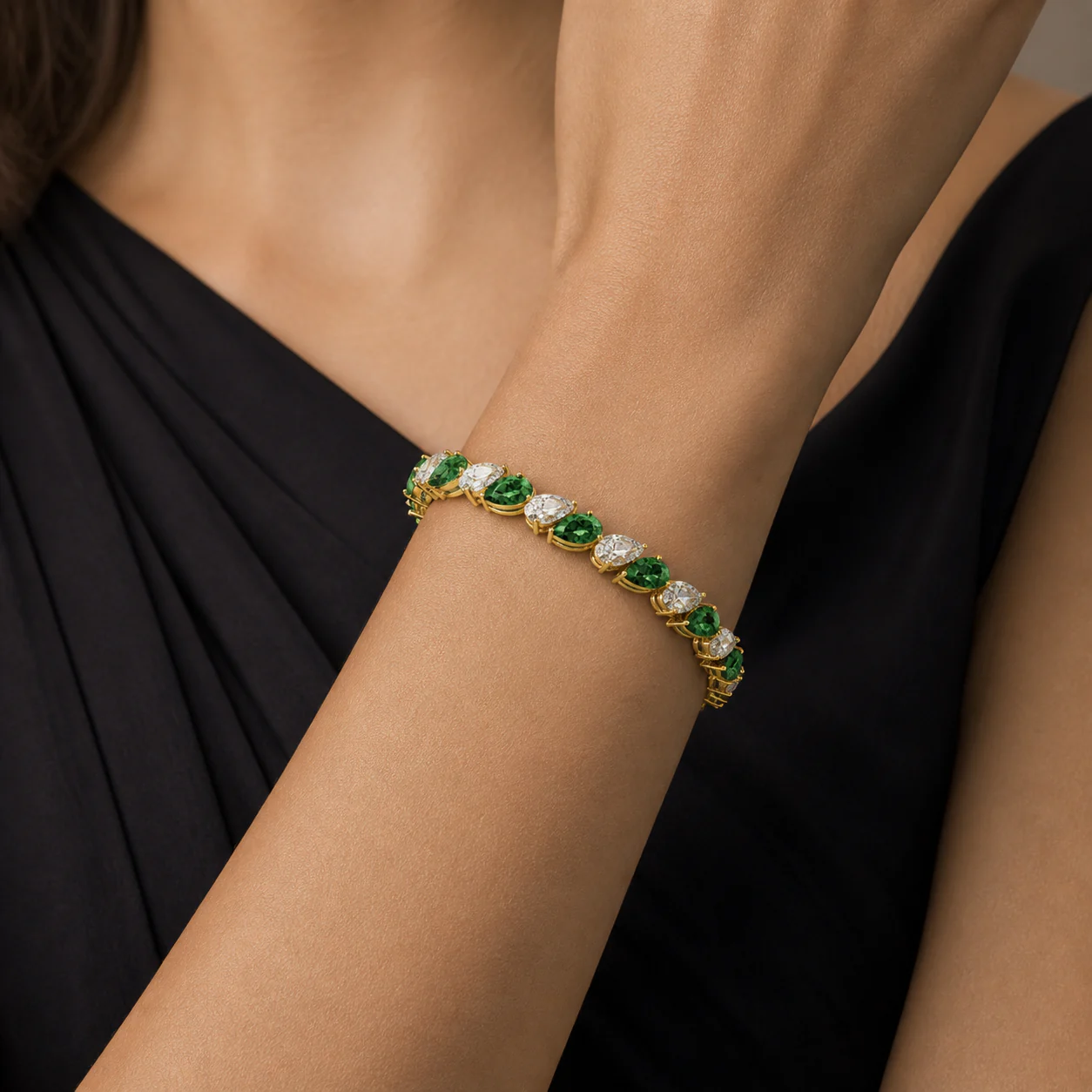 Gold bracelet with vivid green stones and pear-shaped accents worn on the wrist